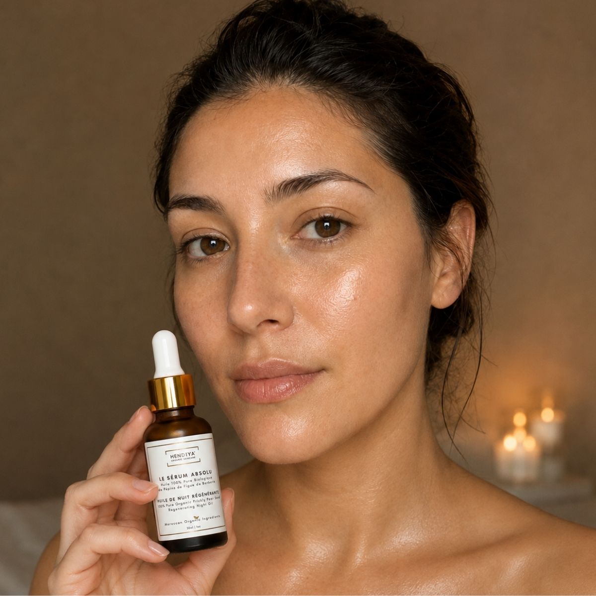Woman holding the Le Sérum Absolu Hendiya® bottle in a candlelit evening ritual setting, prickly pear seed oil